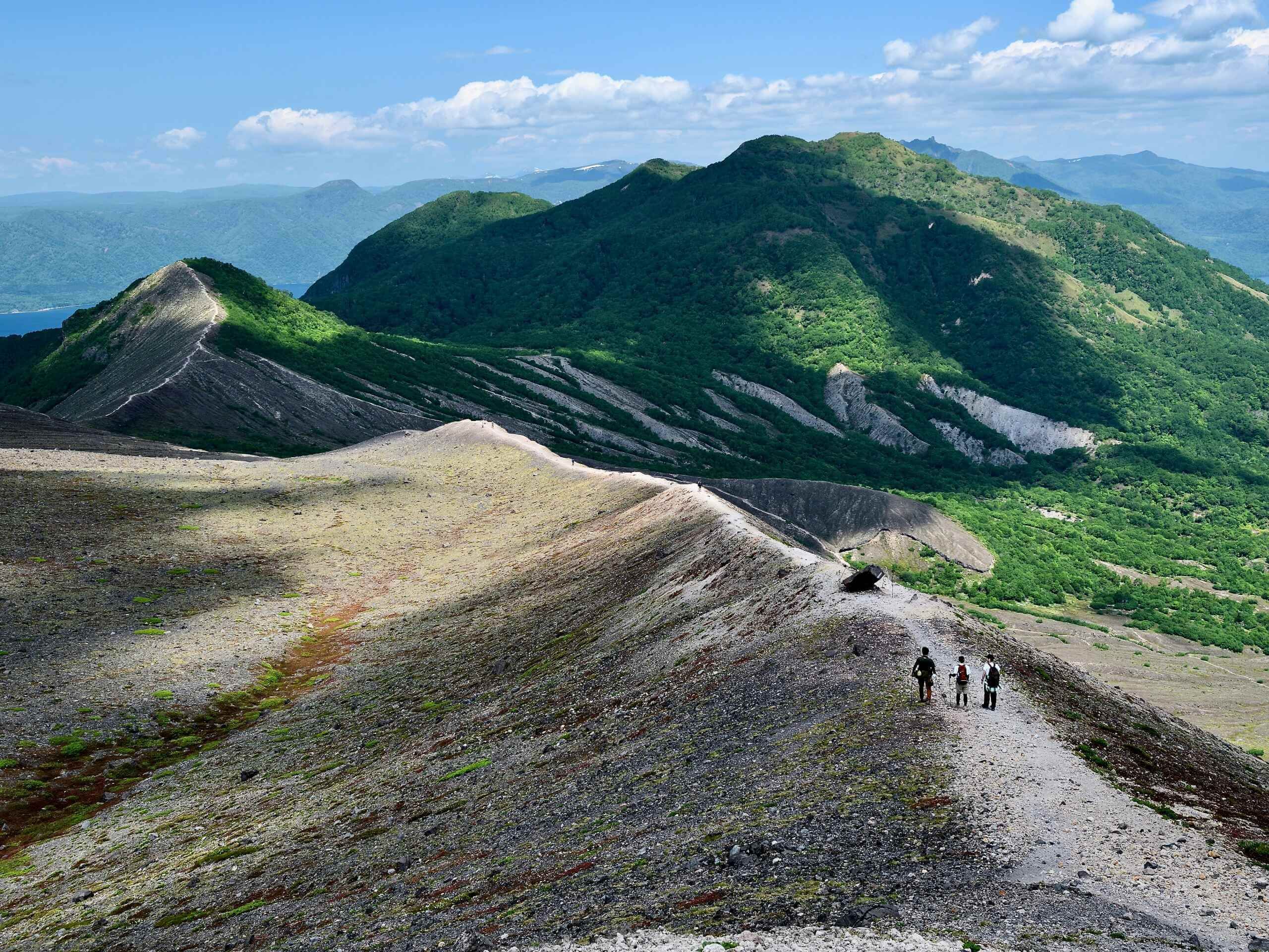 Hikers walking along a ridge toward green mountains in Japan
